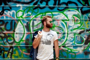 blond man with a beard wearing blue jeans and a white t-shirt , standing against a graffiti wall