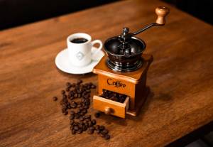 Manual coffee grinder and ceramic cup on rustic wooden table with roasted beans