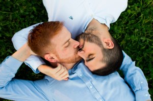 Same-sex couple kissing on grass.