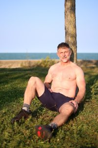 Shirtless man in his 50s sitting by the water