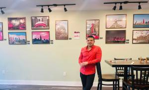 Adrian Sanchez-Iorio standing in front of his "Chicago in Pink" photography exhibition at The Lanzaga Restaurant, displaying framed prints of pink-themed Chicago landmarks.