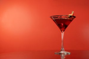 Red cocktail in a martini glass with a strawberry garnish.