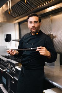 Chef and owner in a professional kitchen, holding a honing steel.